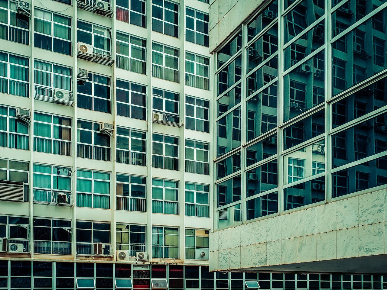 Converging urban buildings with reflective glass and numerous windows seen from below.
